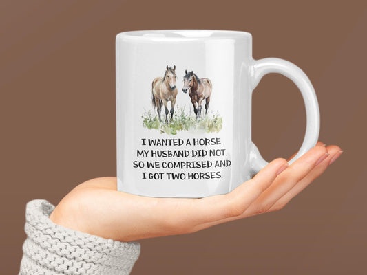 a woman holding a coffee mug with two horses on it